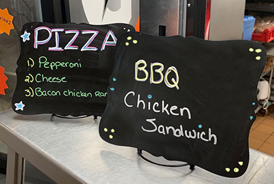 Signs reading Pizza 1. Pepperoni 2. Cheese 2. Bacon Chicken Ranch and BBQ Chicken Sandwich